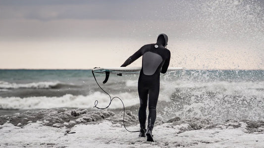 4 best winter wetsuits for surfing with a surfer carrying a surfboard