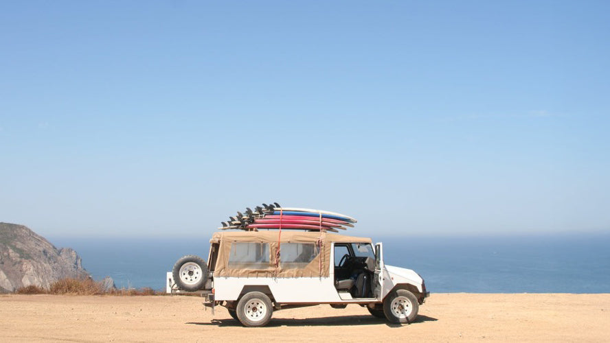 4wd parked ona beach with surfboards stacked on the roof