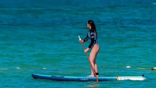 How to stand up on a paddleboard text - with a lady standing up on a paddleboard in blue water